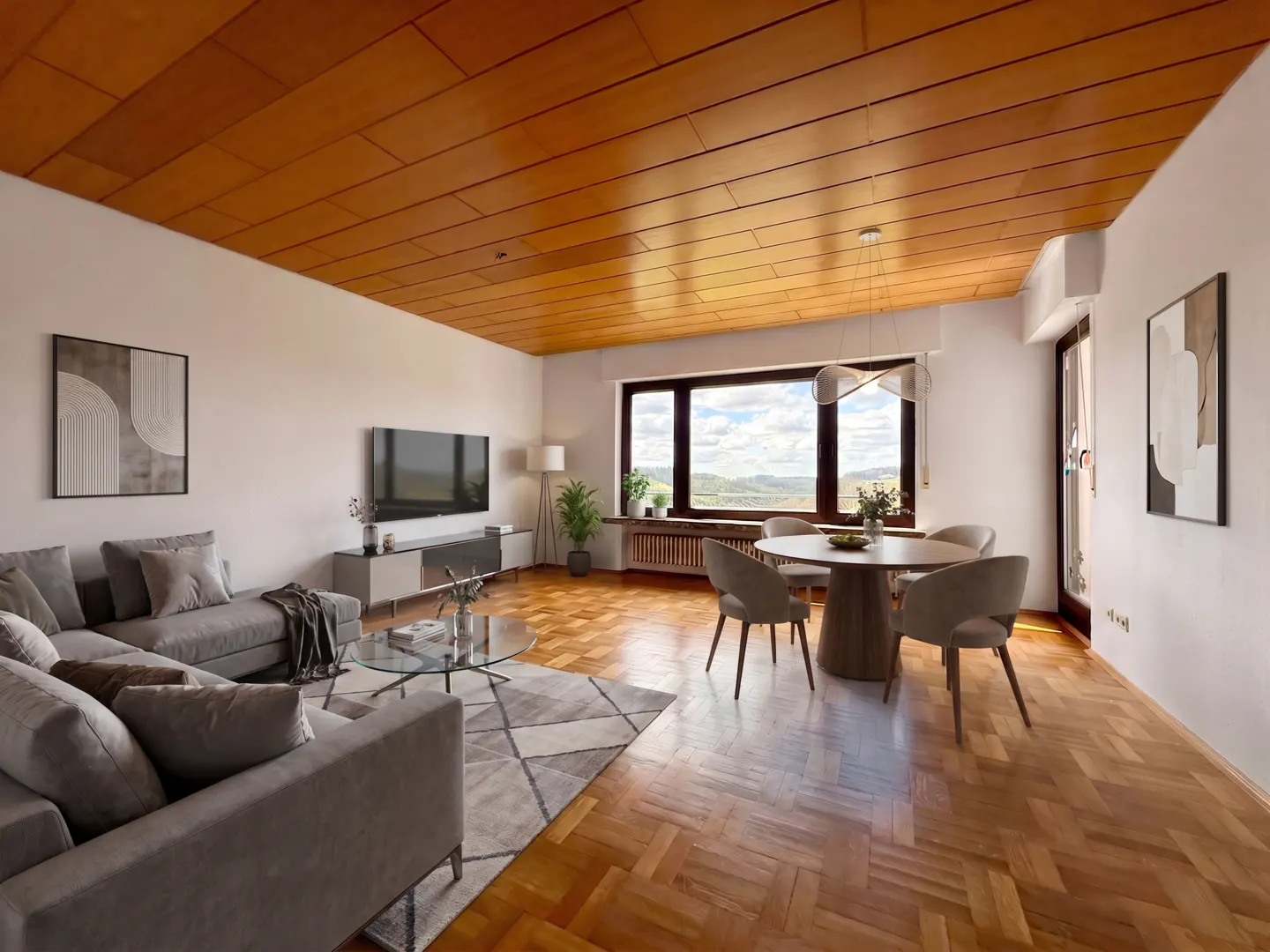 A bright living room with a gray sectional sofa, a round dining table, and a large window with a view.