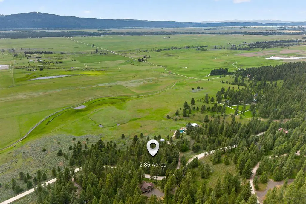Aerial view of 2.85 acres of land with a house surrounded by green trees and a large green field in the background.