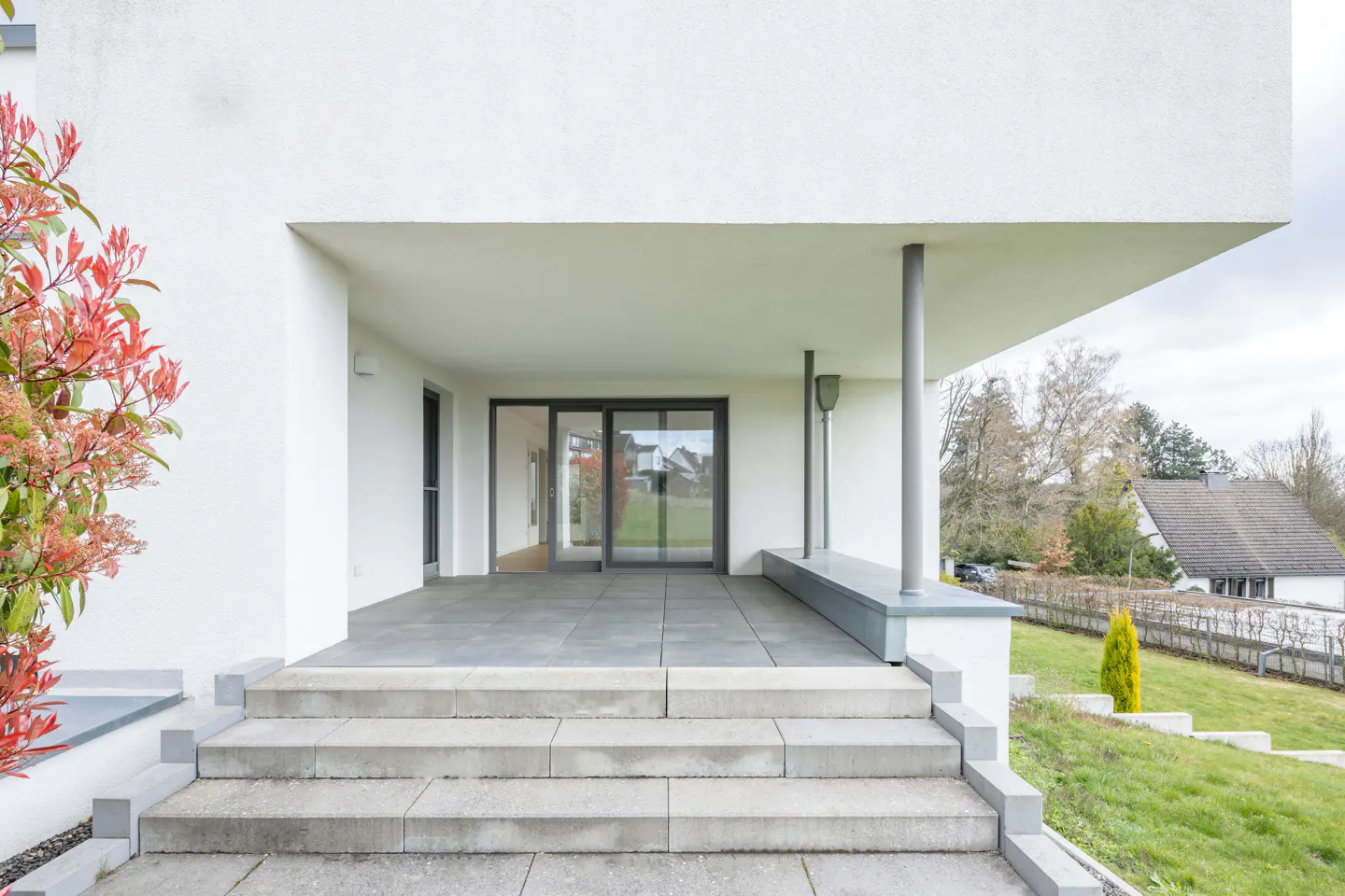 Modern home's entrance with gray stone steps, leading to a covered patio with sliding glass doors and white walls.
