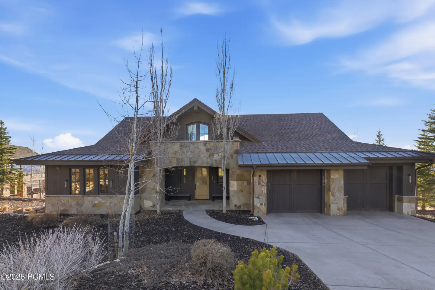 Exterior view of a stone and brown house with a three-car garage and a curved walkway. Blue sky in the background.