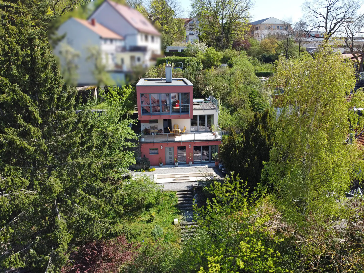 Two-story house with red trim, surrounded by green trees on a hillside. A pool is visible in front.