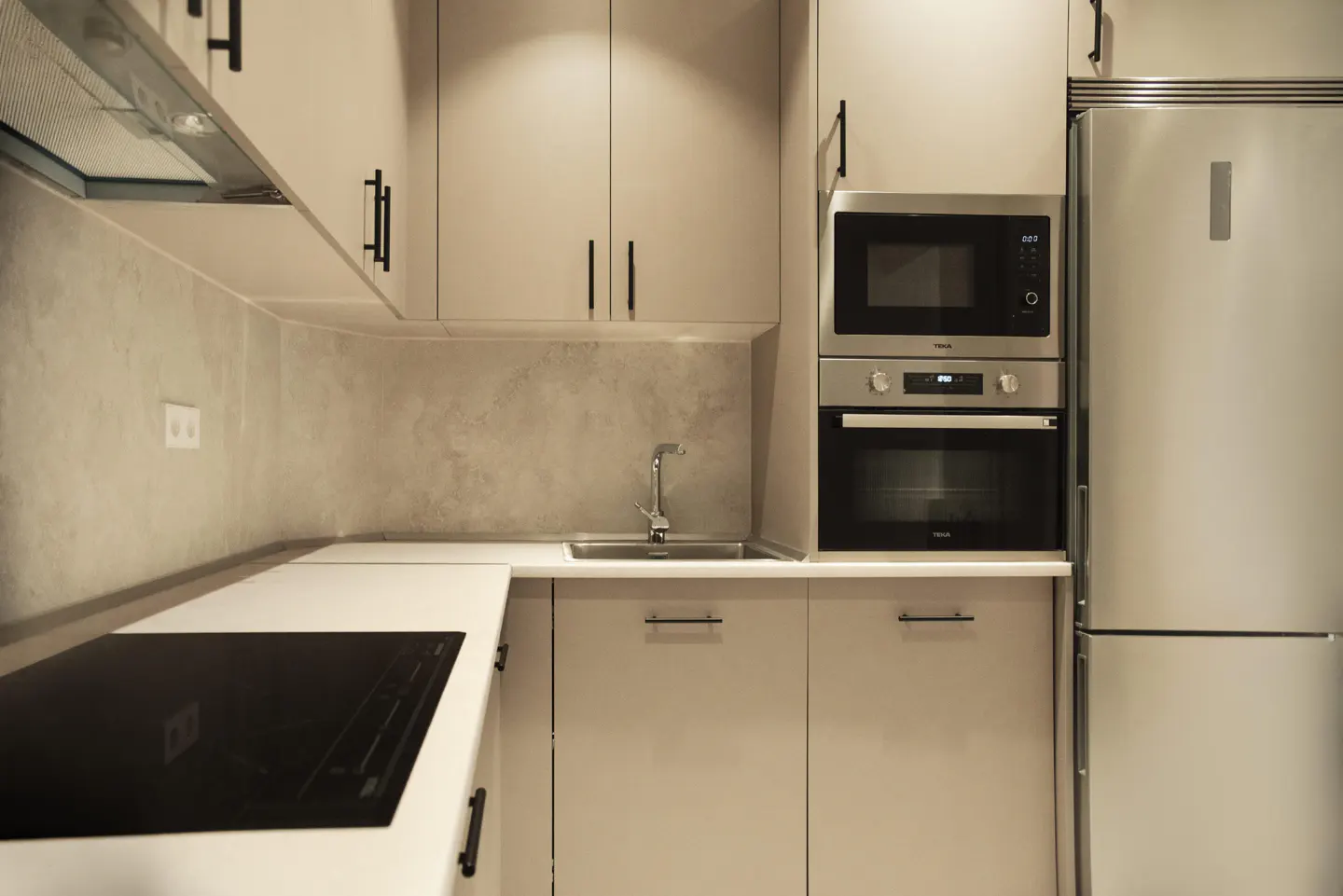 A modern kitchen with beige cabinets, black handles, stainless steel appliances, and a white countertop.