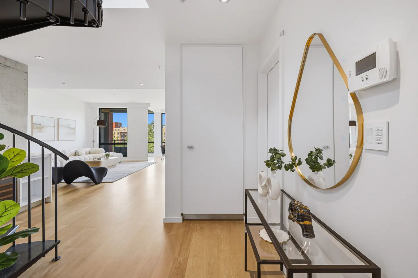 Modern entryway with a glass console table, teardrop-shaped gold mirror, and a view into a bright, open-plan living room.