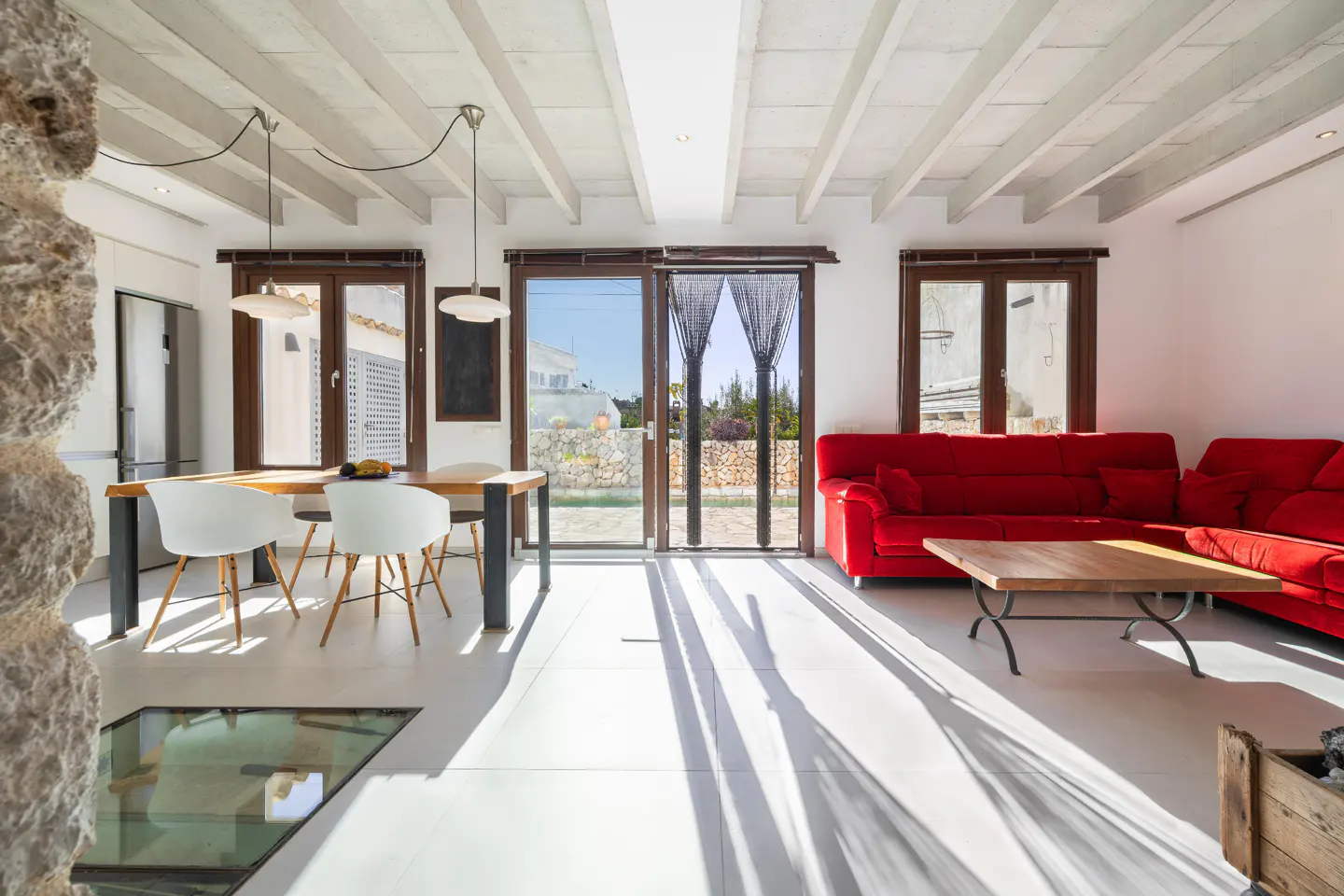 Bright, modern living space with a red sofa, wood table, and white chairs. Large windows offer outdoor views.