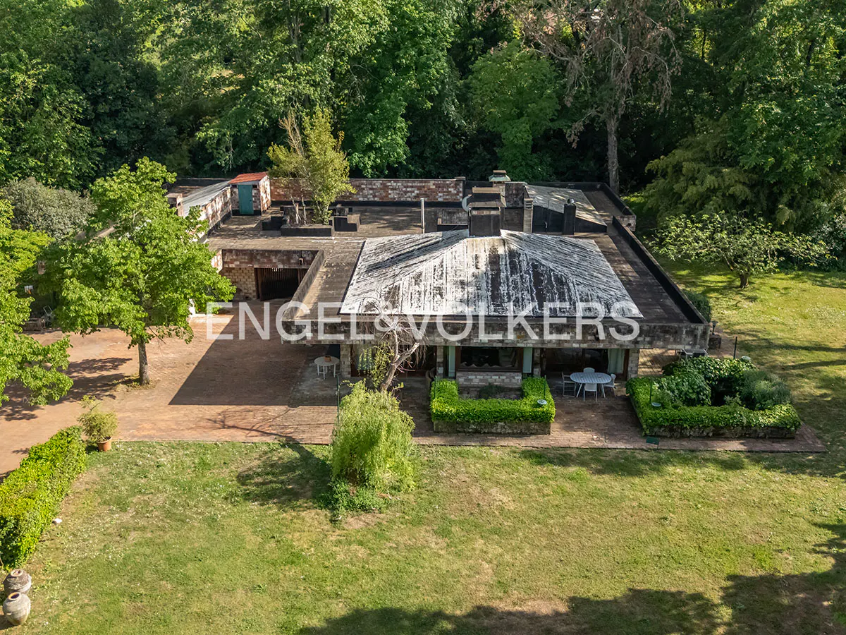 Aerial view of a flat-roofed house with the Engel & Volkers logo, surrounded by green lawns and trees.