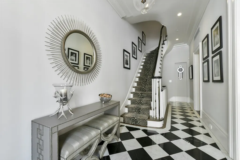 Elegant foyer with black and white checkered floors, a console table with a sunburst mirror, and a staircase with patterned carpet.