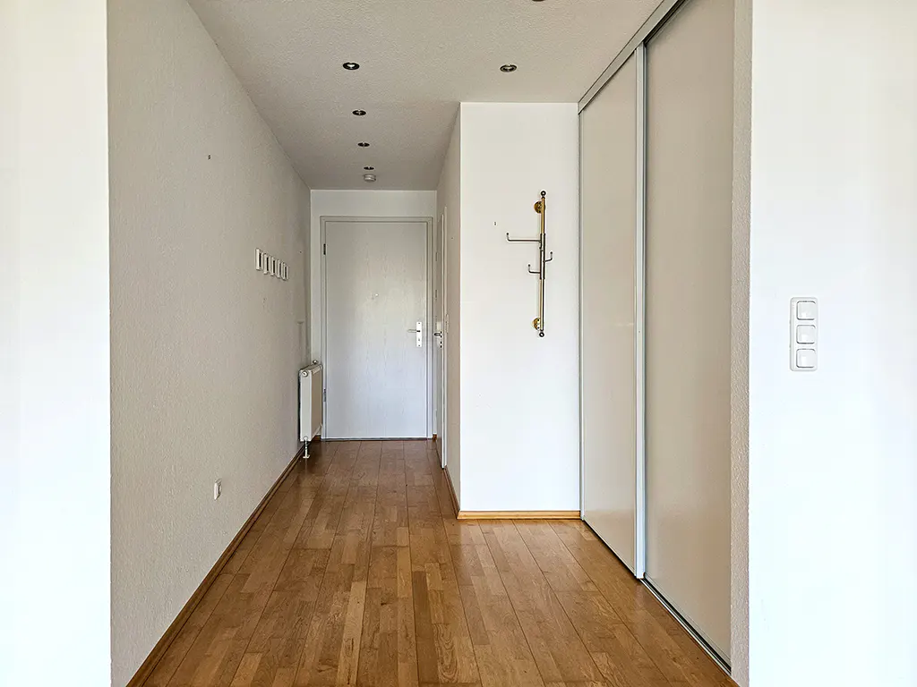 Bright hallway with wood flooring, white walls, a white door, a wall-mounted coat rack, and large sliding closet doors.