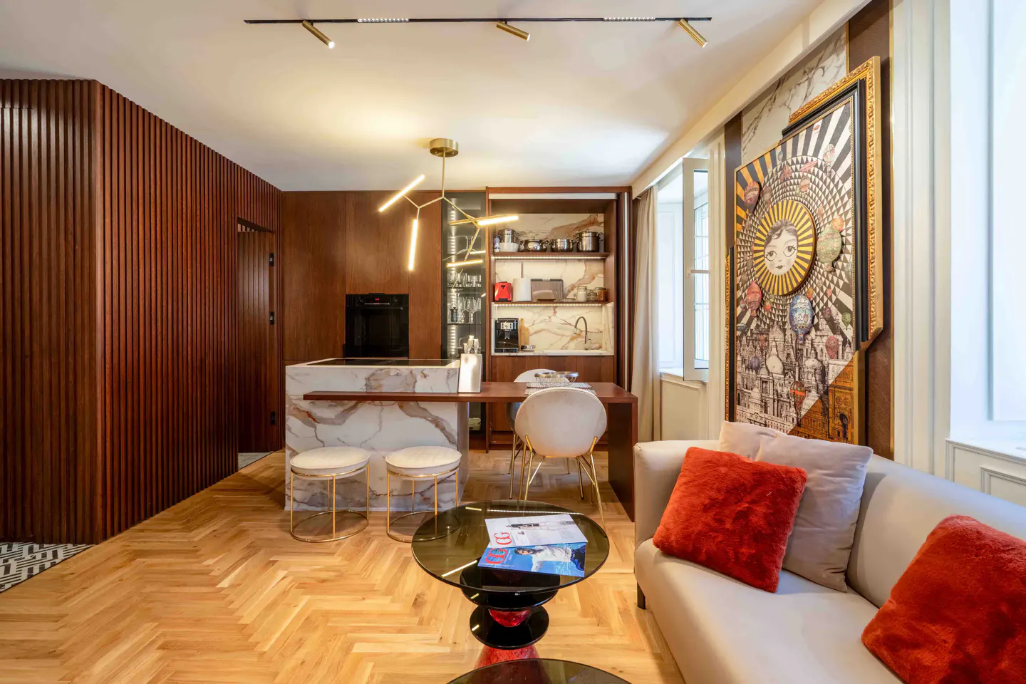 Modern apartment with wood-paneled walls, marble kitchen island, dining area, and a sofa with orange pillows.