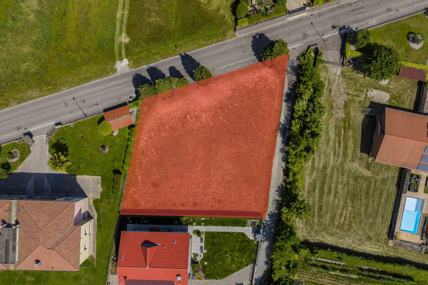 Aerial view of a vacant plot of land highlighted in red, situated between residential houses and a road.