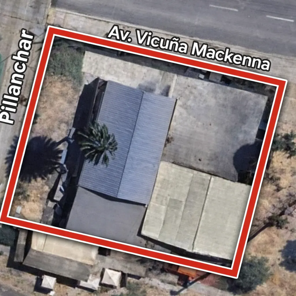 Aerial view of a property outlined in red, showing buildings with gray roofs, a concrete yard, and nearby streets.