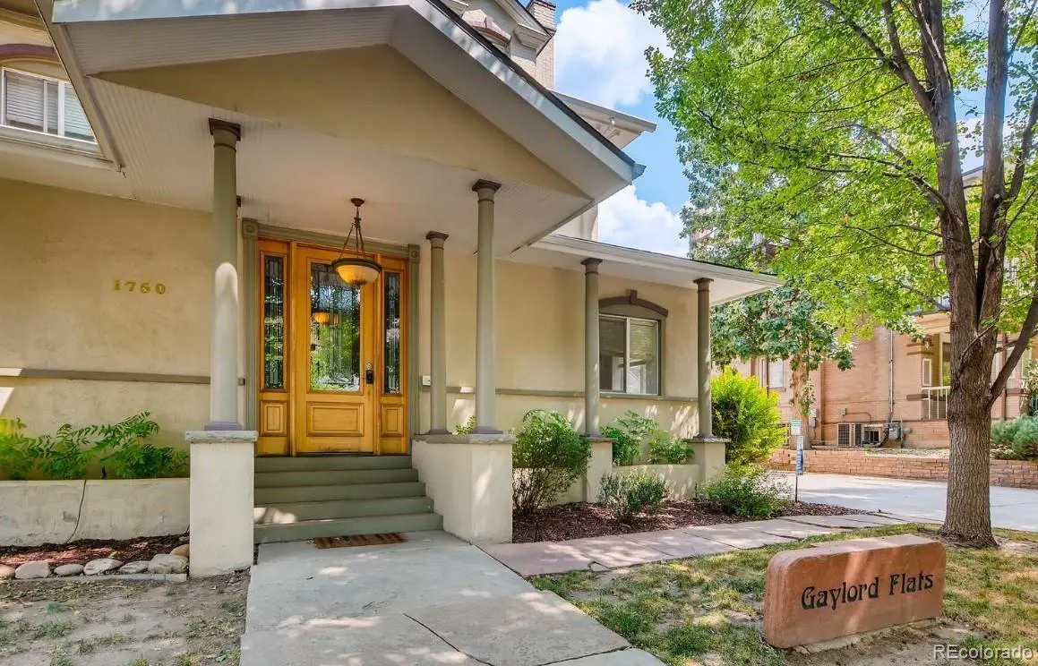 Exterior view of Gaylord Flats with a yellow door, columns, and a stone sign on the lawn.