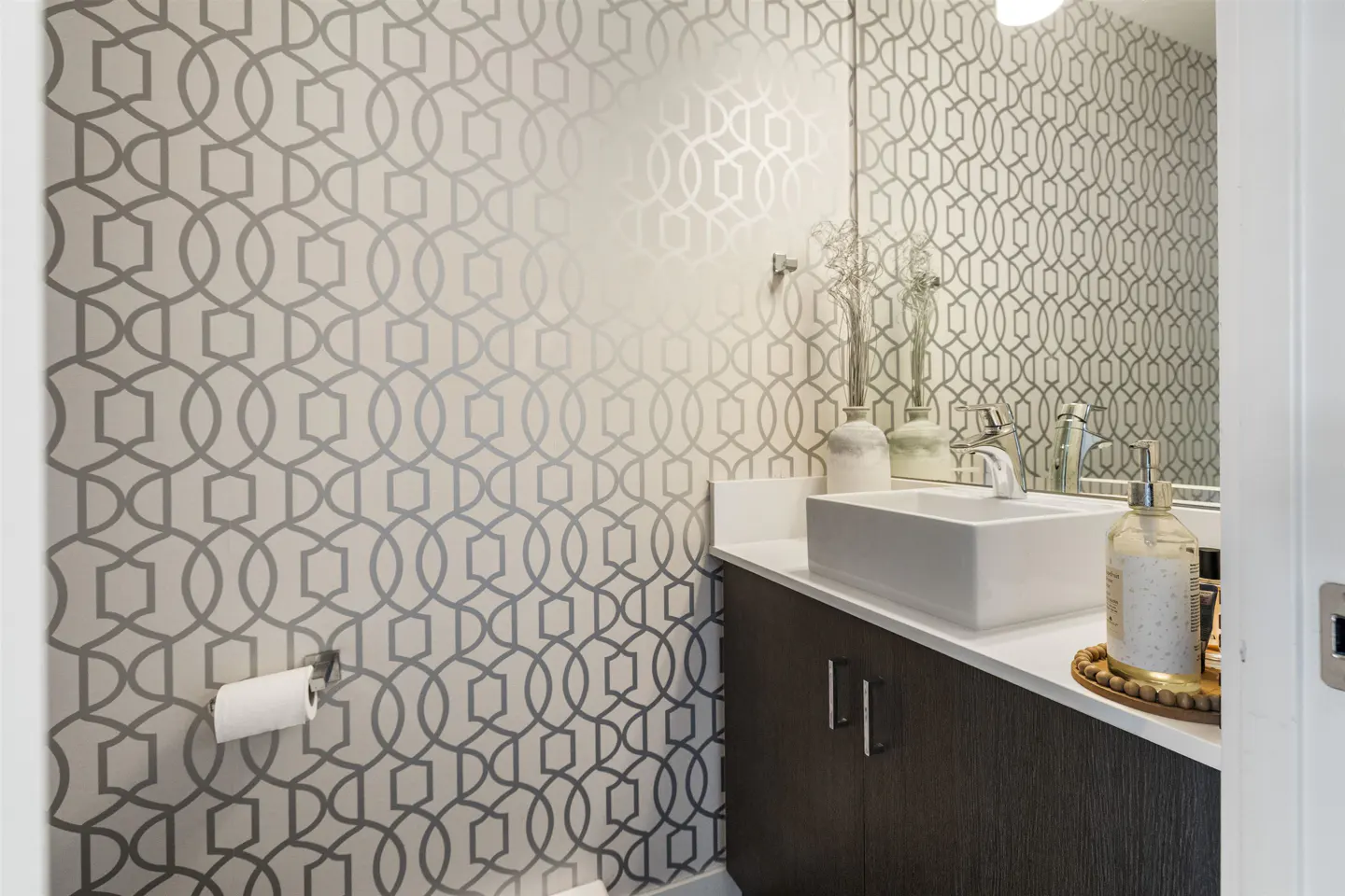 A modern powder room with geometric wallpaper, a white rectangular sink, and a dark wood vanity.