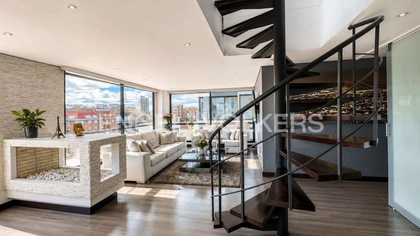Bright living room with a spiral staircase, white sofas, and a modern fireplace. Large windows offer city views.