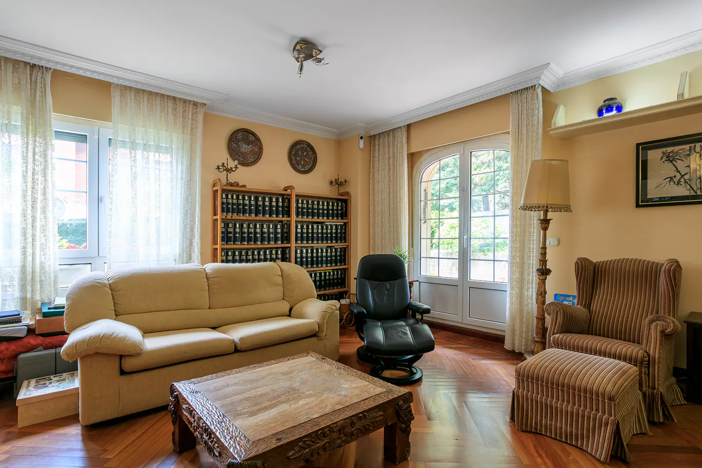 Living room with a beige sofa, black recliner, striped armchair with ottoman, and a wooden coffee table on a herringbone floor.