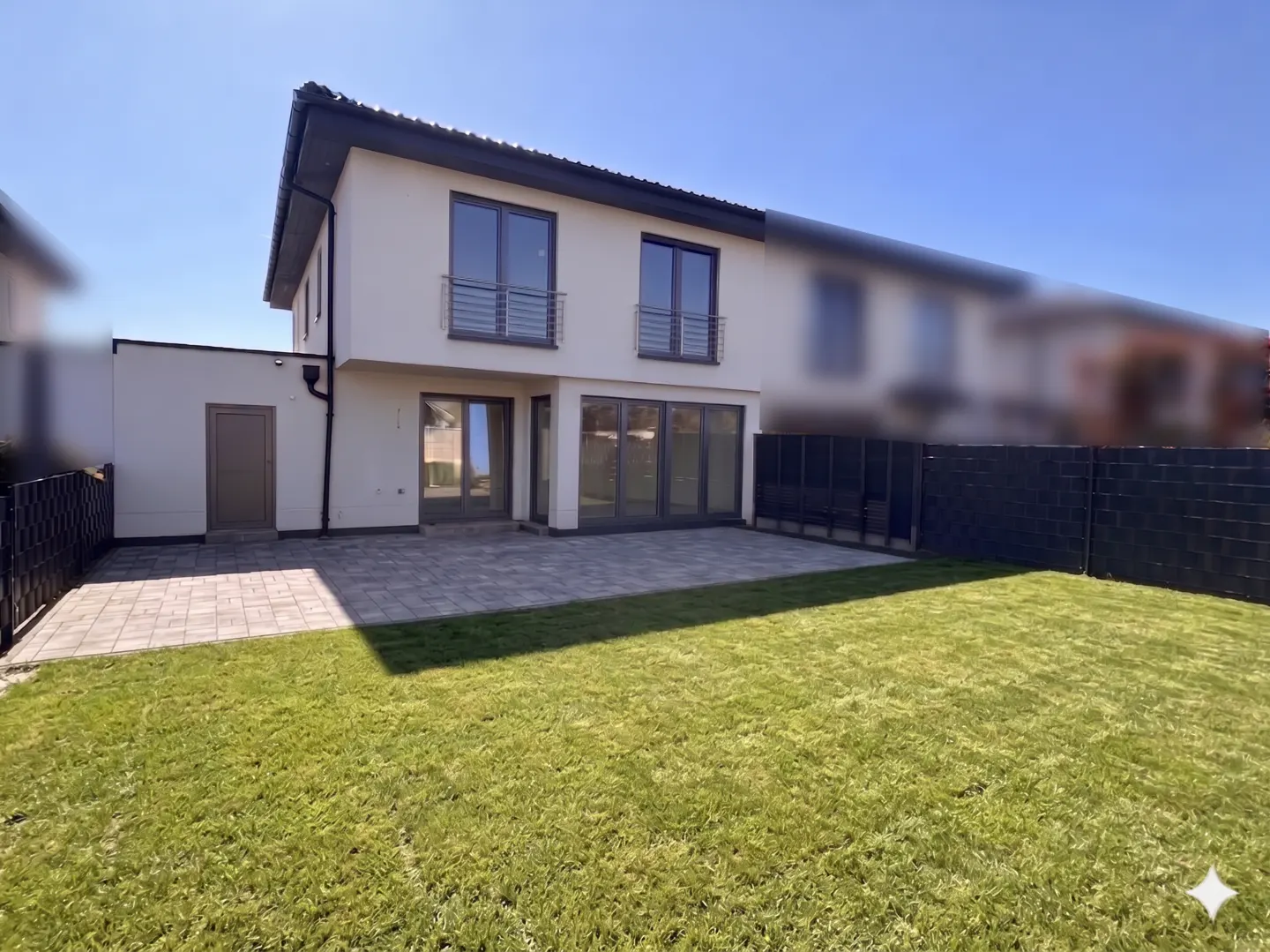 Two-story house with a gray patio, green lawn, and black fence under a blue sky.