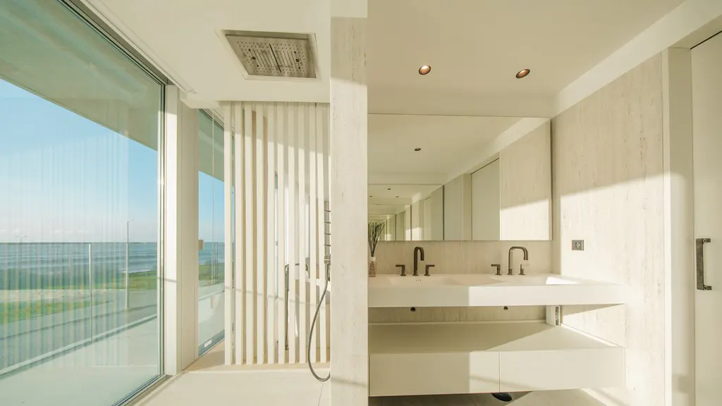 Bright, modern bathroom with a double sink, large mirror, and a shower with a view of the ocean.