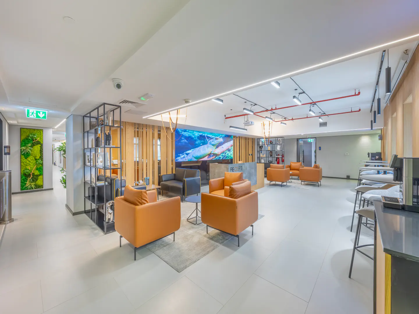 Modern office lobby with orange and black armchairs, a large screen displaying underwater scenery, and a reception desk.