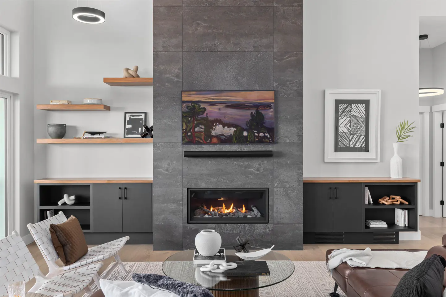 Living room with a gray tile fireplace, TV, and gas fire. Gray cabinets with wood countertops flank the fireplace. A glass coffee table sits on a patterned rug.