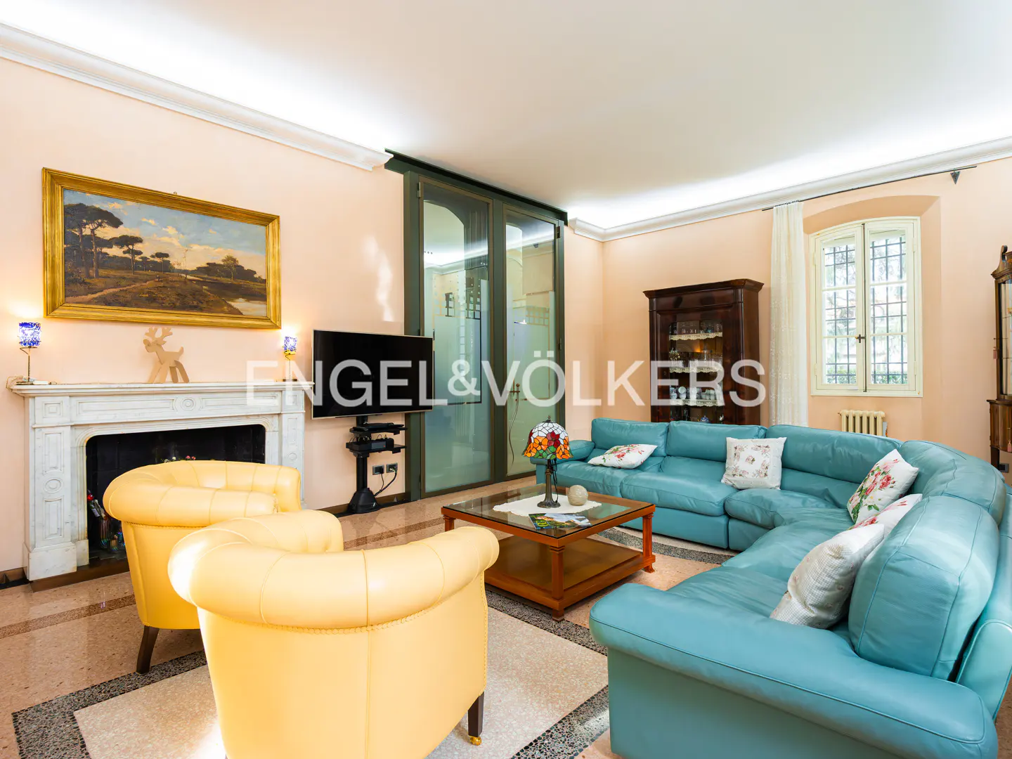 Living room with yellow armchairs, a blue sectional sofa, and a fireplace with a landscape painting above it.