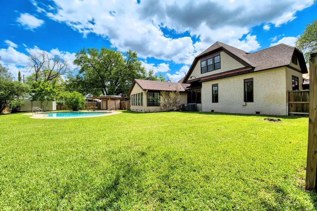 Backyard view of a two-story house with a pool, green grass, and blue sky with white clouds.