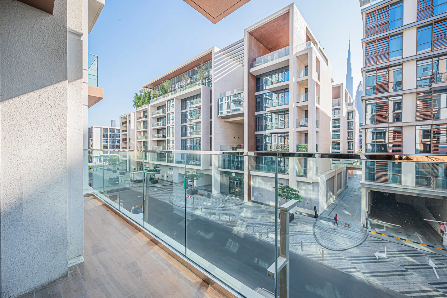 View from a balcony with glass railings overlooking a street with modern buildings and the Burj Khalifa in the background.