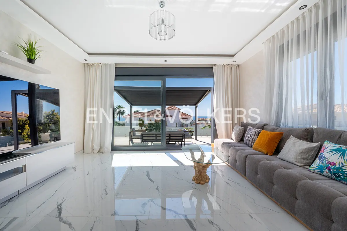 Bright living room with marble floors, gray sofa, glass table, and sliding doors to a patio with ocean views.