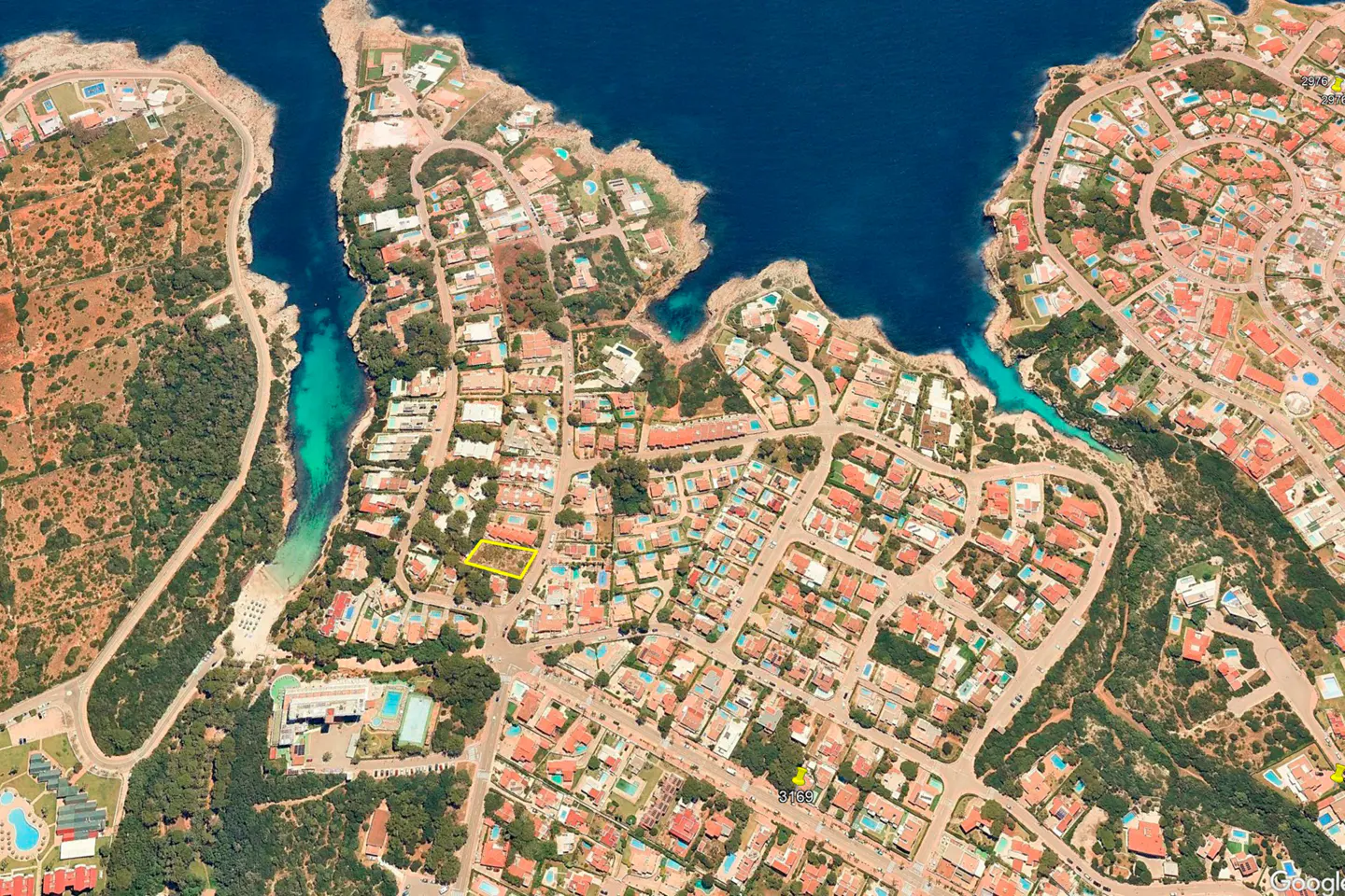 Aerial view of a coastal neighborhood with red-roofed houses, blue ocean inlets, and a property outlined in yellow.