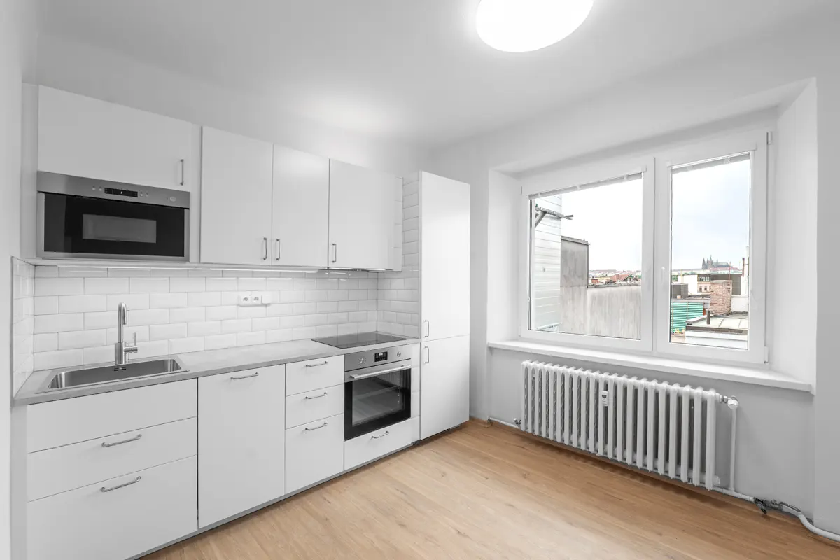 Bright, modern kitchen with white cabinets, stainless steel appliances, and light wood floors. A window overlooks a cityscape.