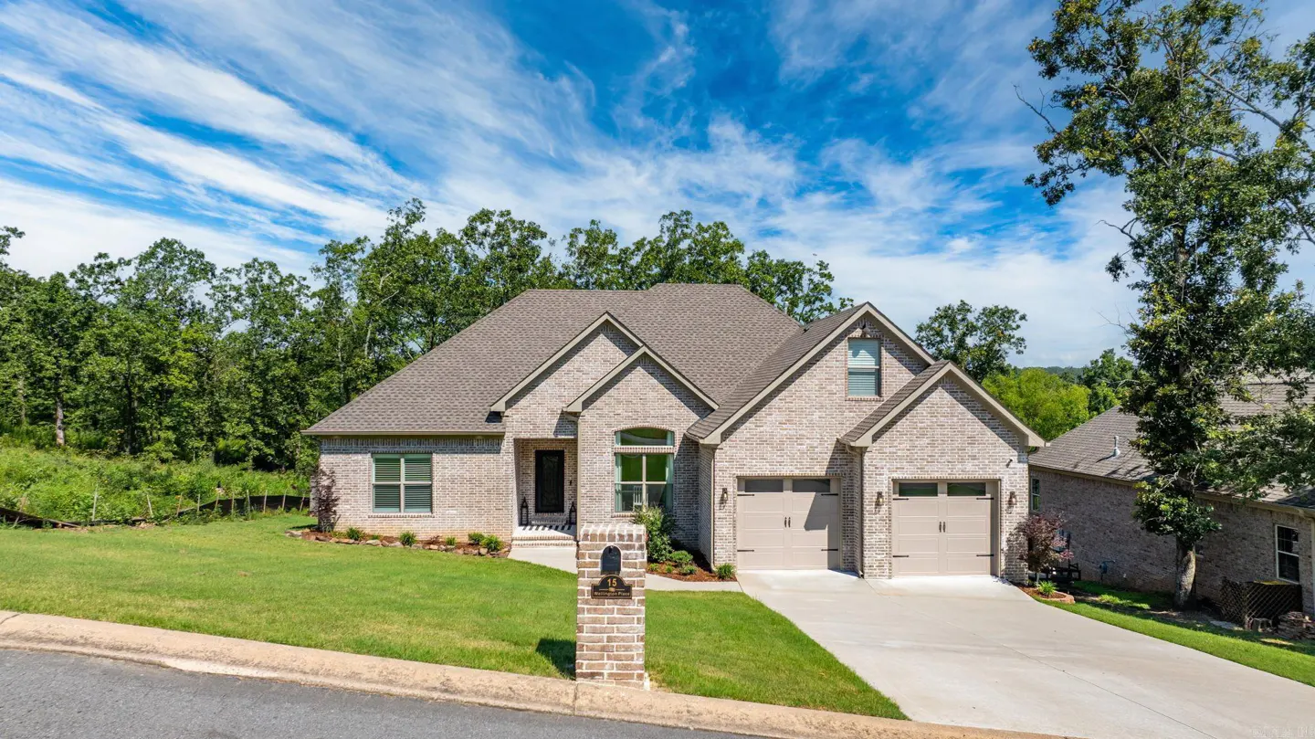 A single-family home with a brick exterior, a gray roof, and a two-car garage on a green lawn under a blue sky.