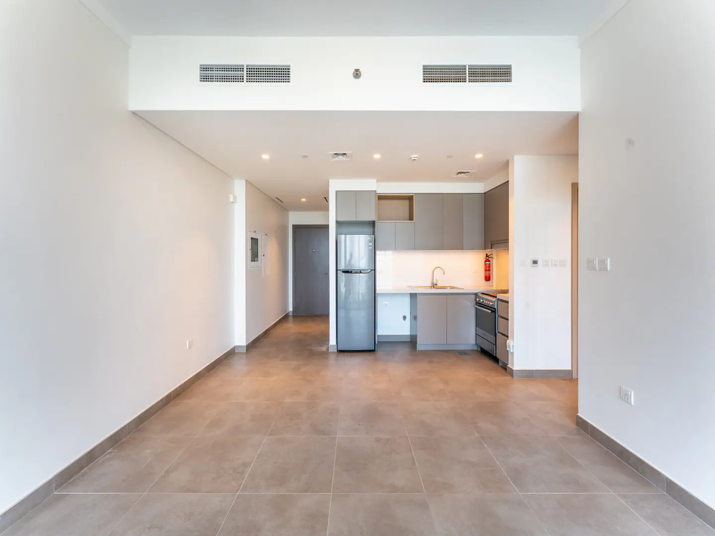 A modern apartment interior with gray cabinets, stainless steel appliances, and tile flooring. The walls are white.