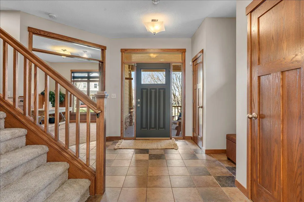 Foyer view with a gray front door, wood trim, and tiled floor. A staircase with carpeted steps is on the left.
