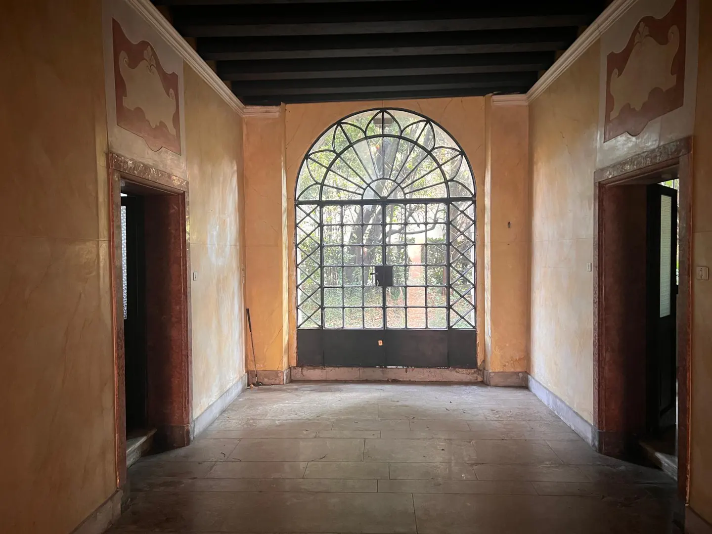 Arched window with black metal frame in a yellow room with two open doorways and dark wood ceiling.