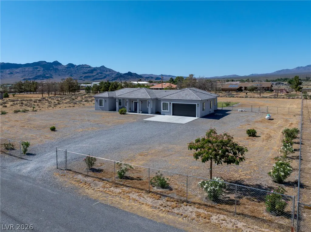 Single-story gray house with a two-car garage on a large, fenced desert lot with mountain views under a clear blue sky.
