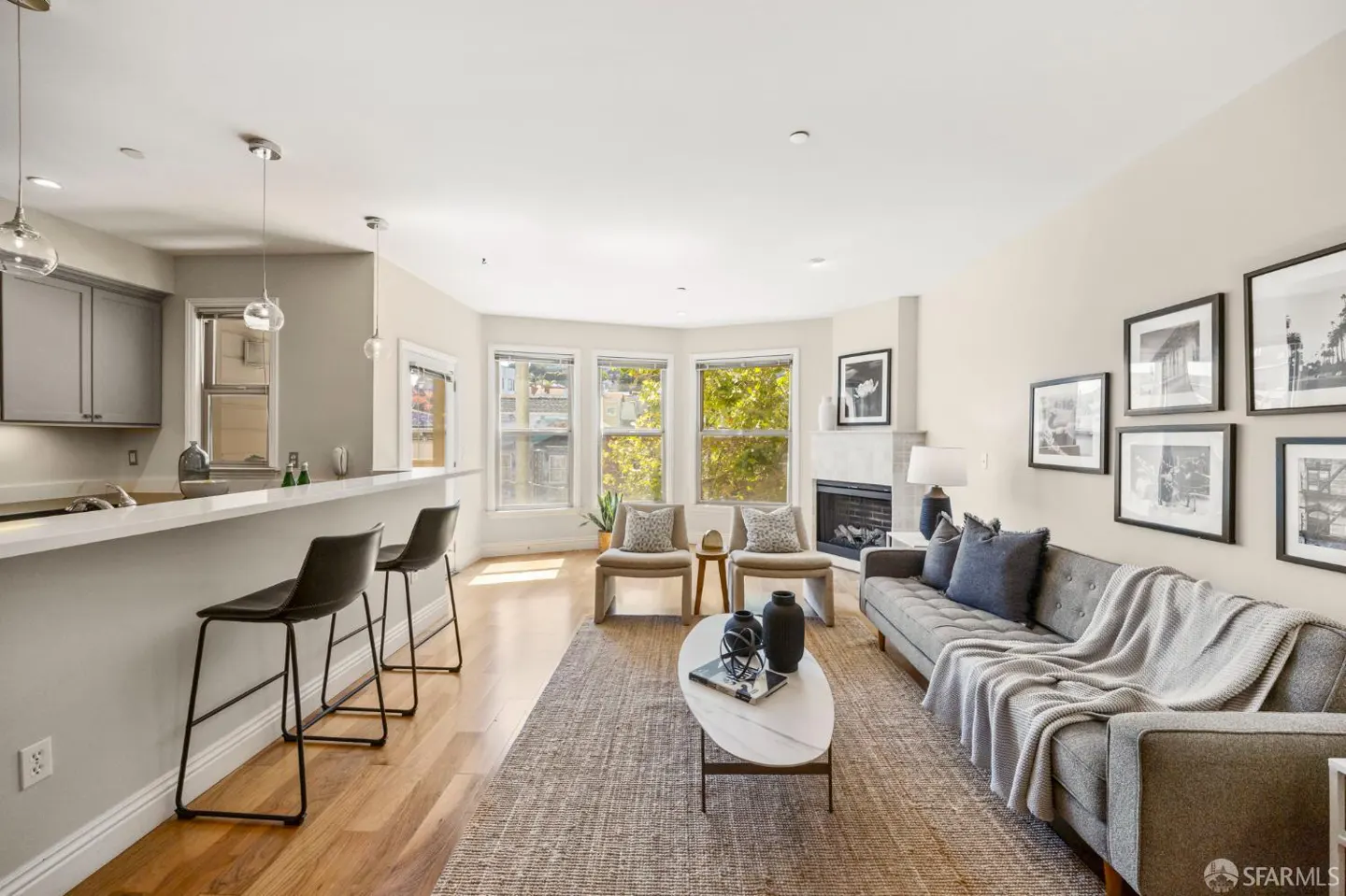 Modern open-concept living room with a grey sofa, two armchairs, a fireplace, and a kitchen breakfast bar with stools.