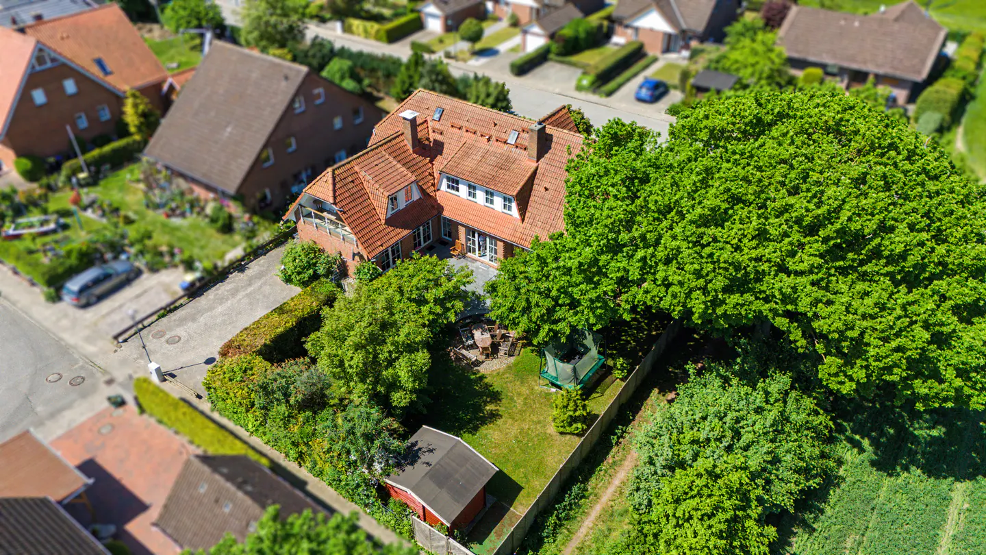 Aerial view of a house with a red-tiled roof, a lush backyard with a trampoline, and a small shed in a suburban setting.