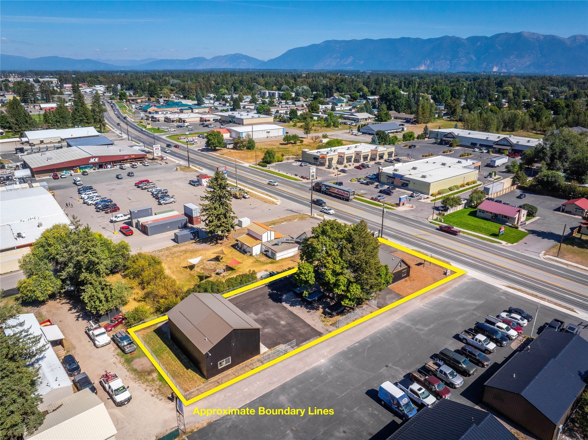 Aerial view of a commercial property outlined in yellow, featuring a dark building, parking, and nearby retail businesses. [AI-generated text]