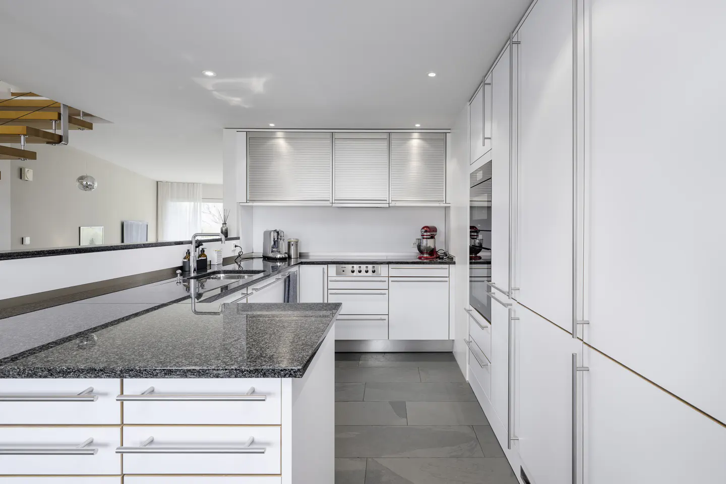 Bright, modern kitchen with white cabinets, granite countertops, and stainless steel appliances. Gray tile floor and open floor plan.