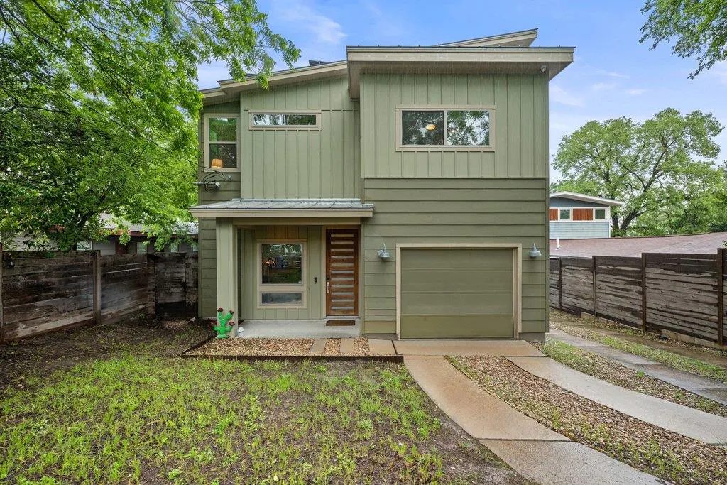 Two-story, light green house with a garage, a wooden front door, and a concrete driveway with gravel strips.