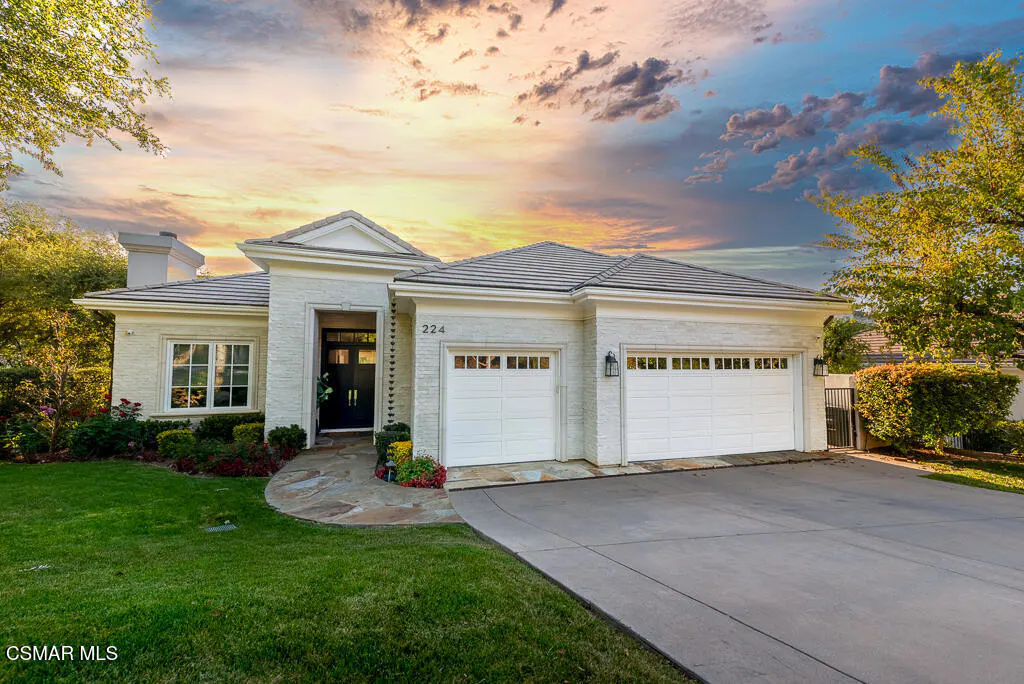 Exterior view of a one-story white brick house with a gray roof, two-car garage, and green lawn.