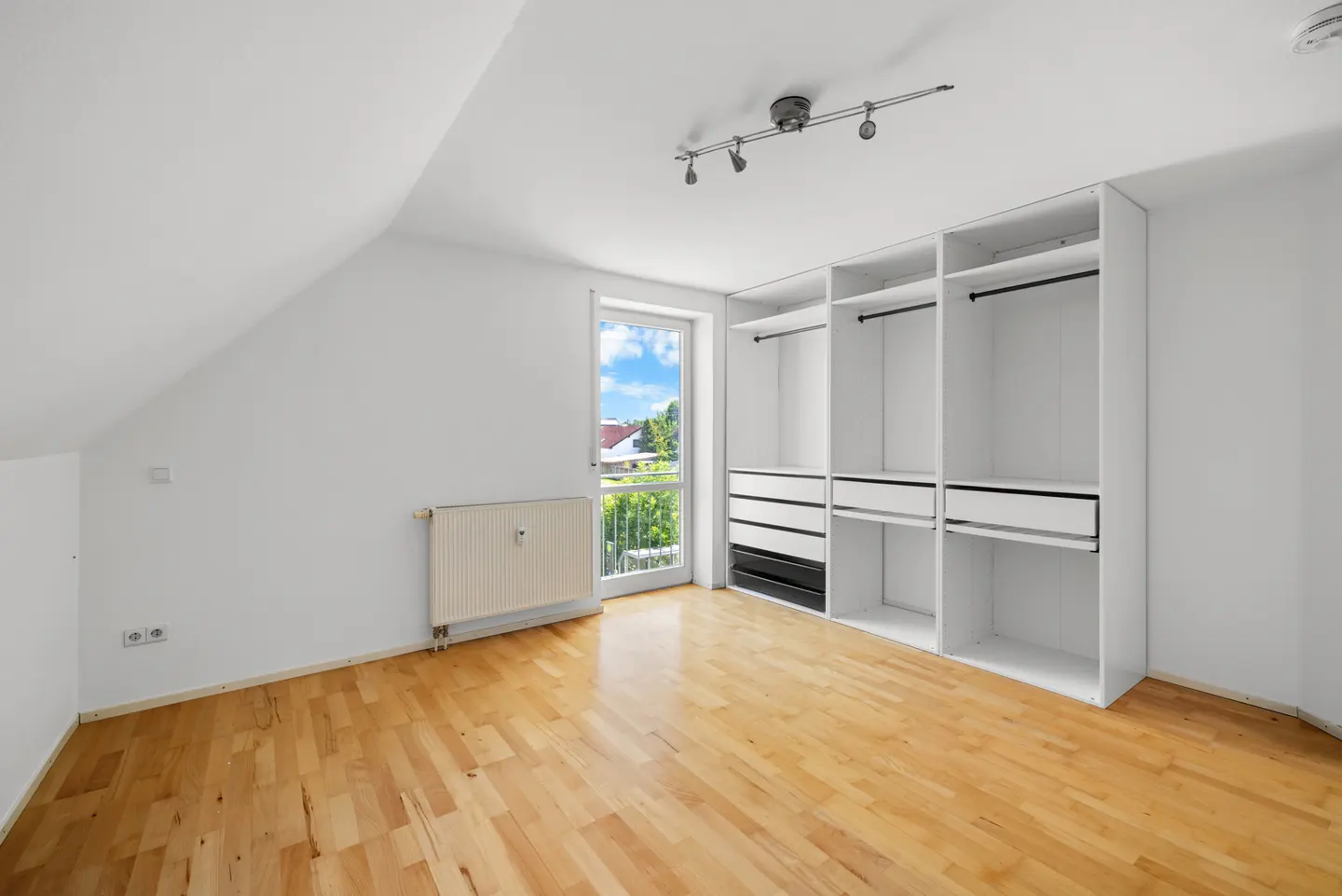 Bright room with light wood floors, white walls, a large built-in wardrobe, a radiator, and a glass door to a balcony.