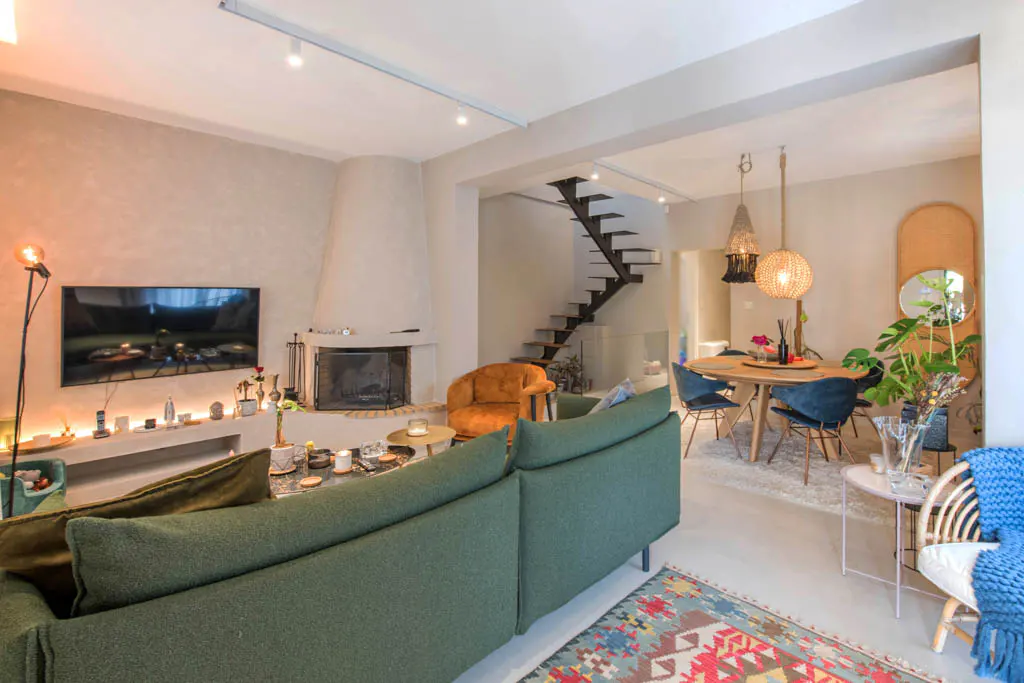 A bright, open-concept living and dining area with a green sofa, fireplace, TV, and a dining table with blue chairs.