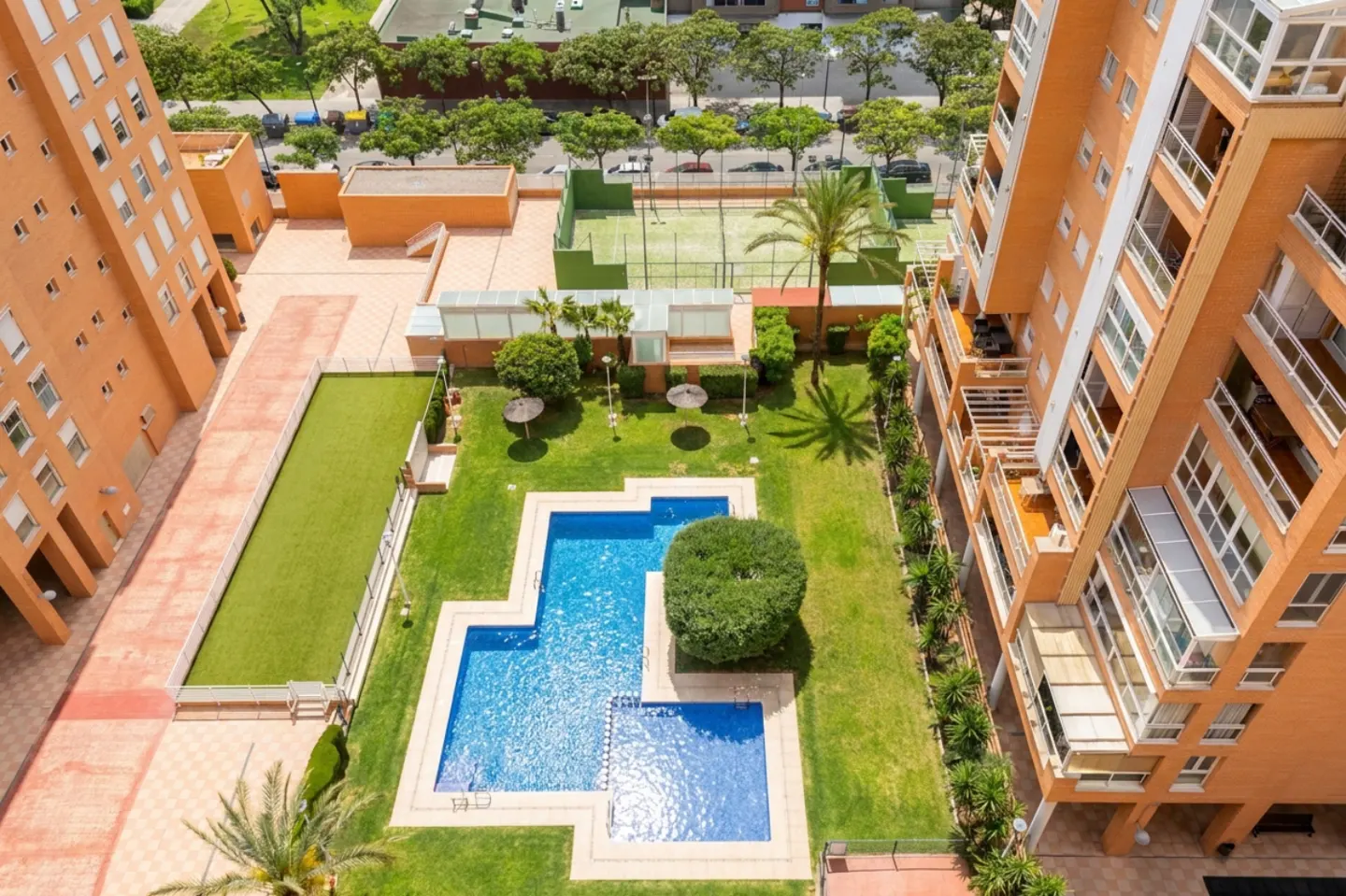 Aerial view of a complex with orange buildings, a blue pool, green lawn, and a tennis court.