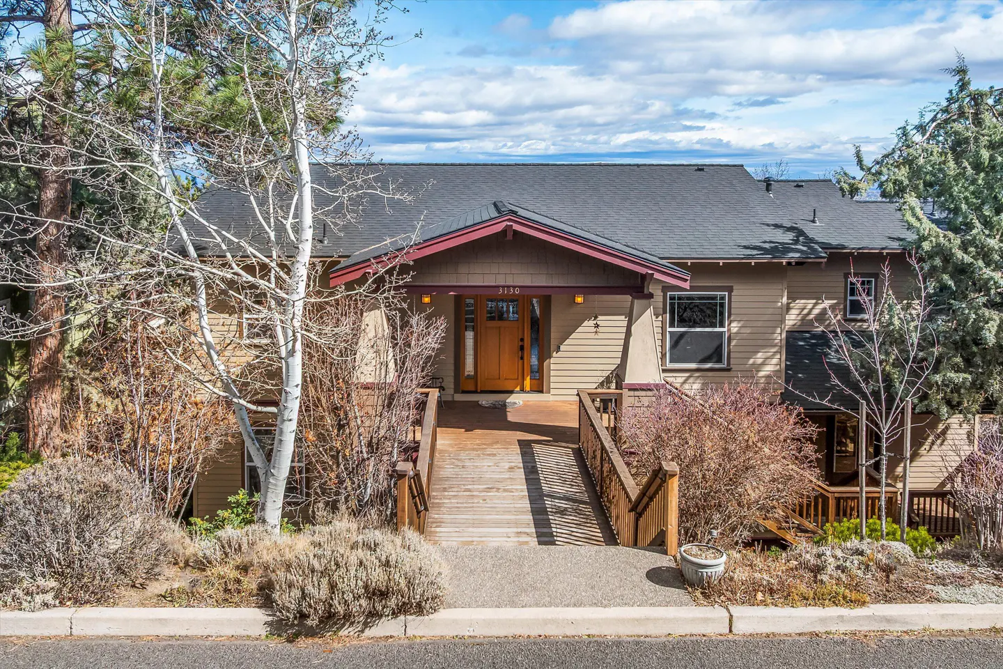 Exterior view of a two-story beige house with a gray roof and a wooden ramp leading to the front door.