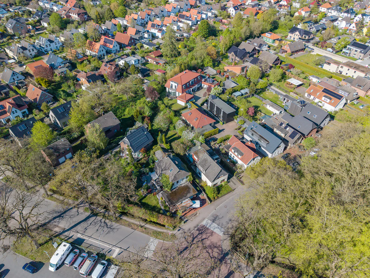 Aerial view of a residential neighborhood with houses, trees, and parked cars on a sunny day.