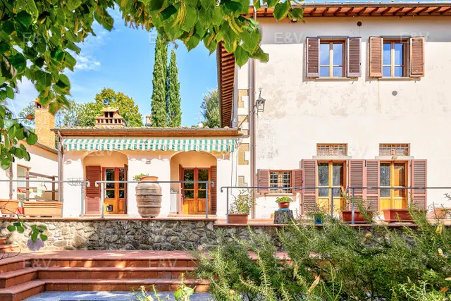 Exterior view of a Tuscan-style villa with stone terrace, brown shutters, and green-striped awning.