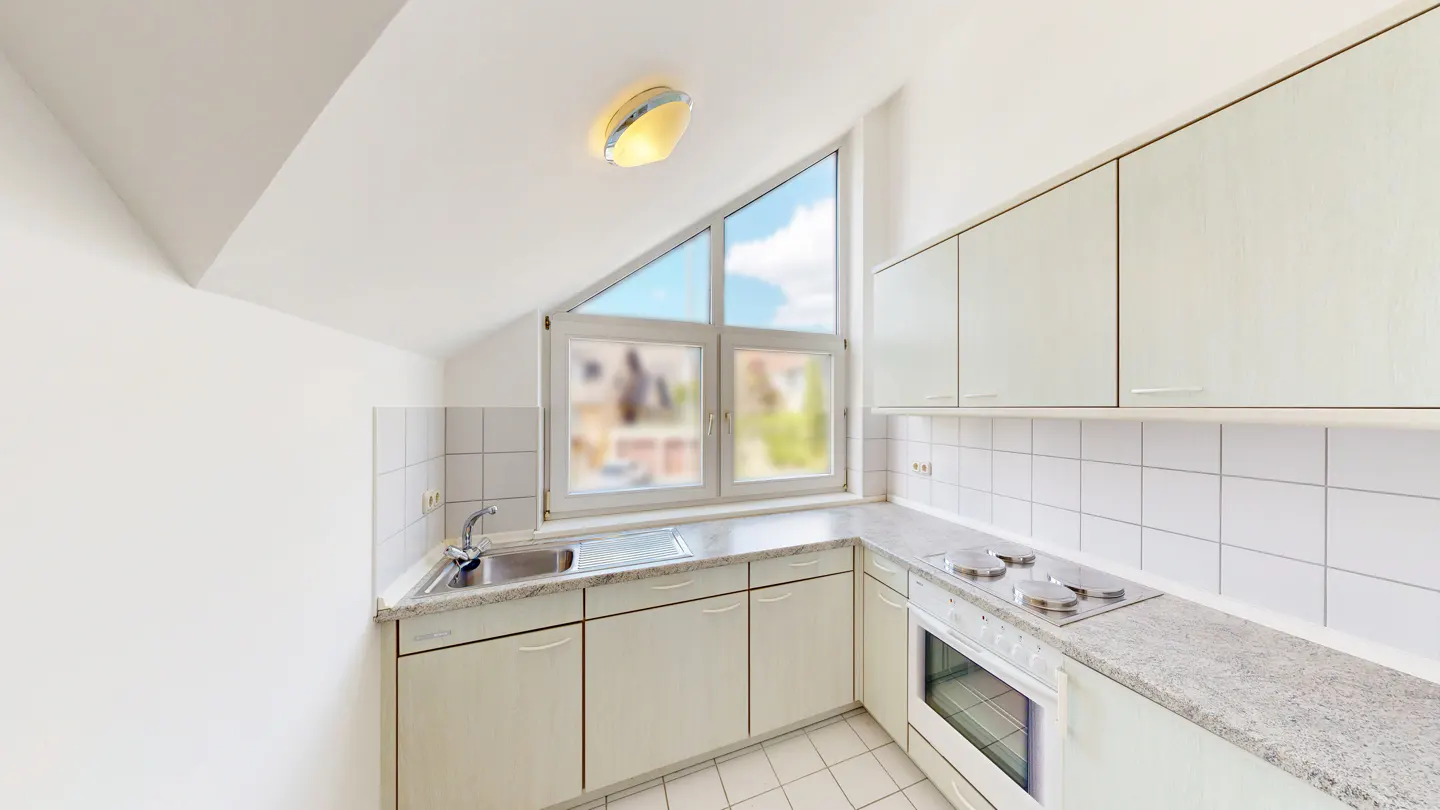 Bright kitchen with white cabinets, tile backsplash, and granite countertops. A triangular window lets in natural light.