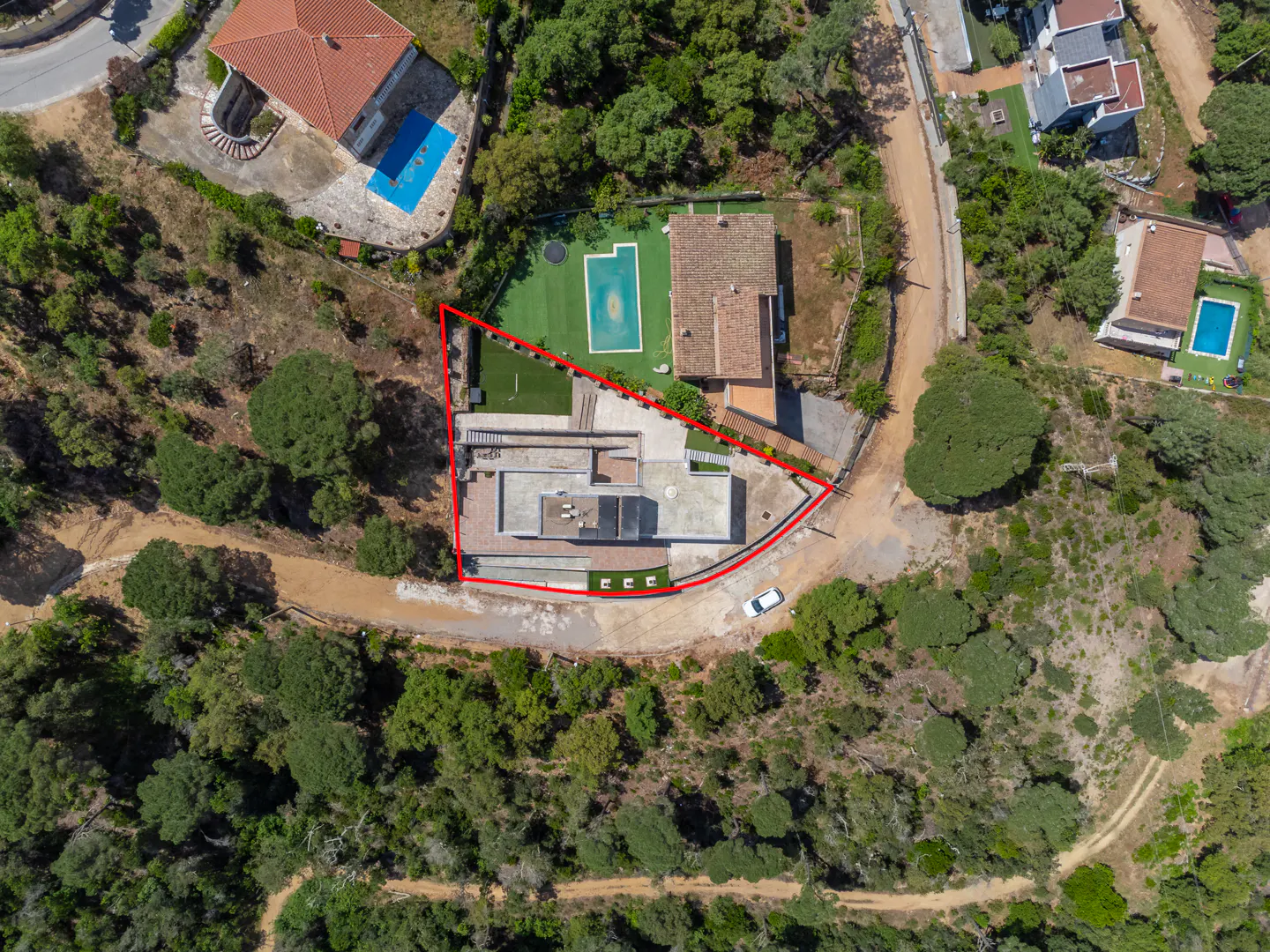 Aerial view of a property with a red boundary line, surrounded by trees. The property includes a house, pool, and lawn.