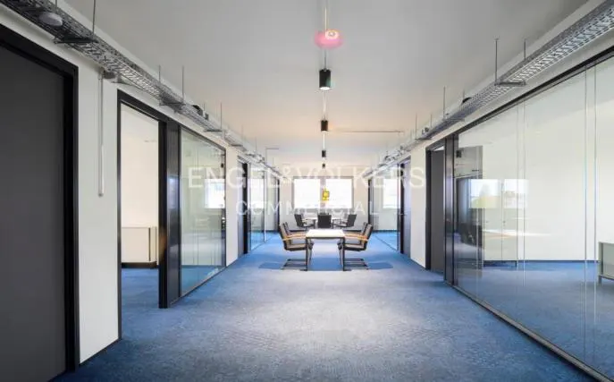 Office space with blue carpet, glass-walled offices, and a conference room with a table and chairs.