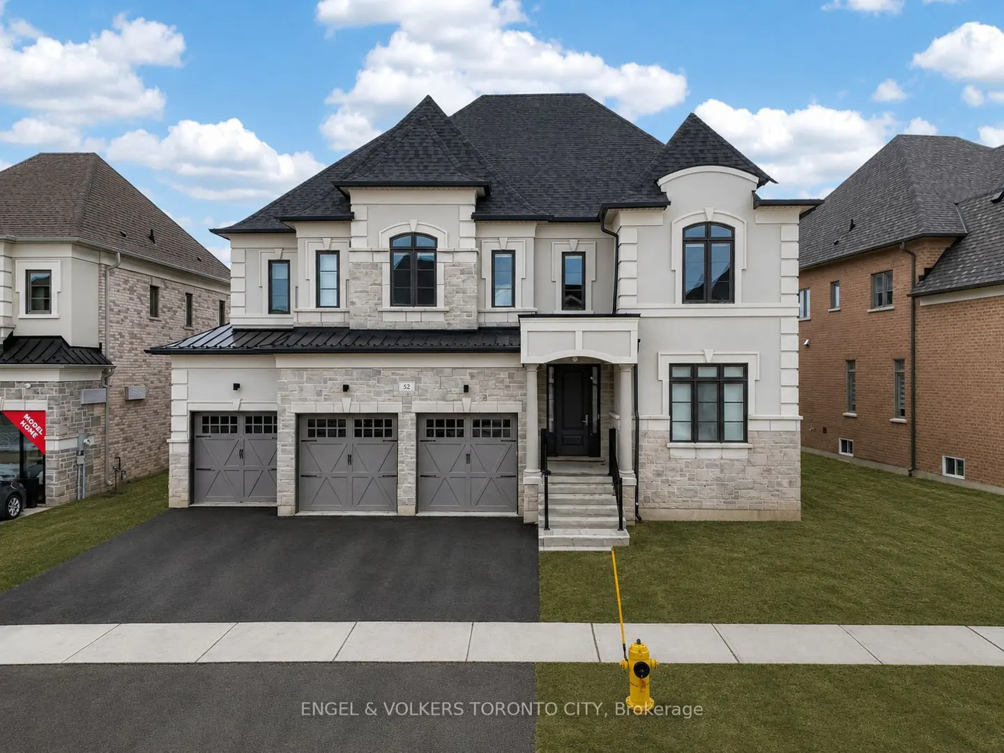 A two-story house with a three-car garage, stone and stucco exterior, and a black roof.