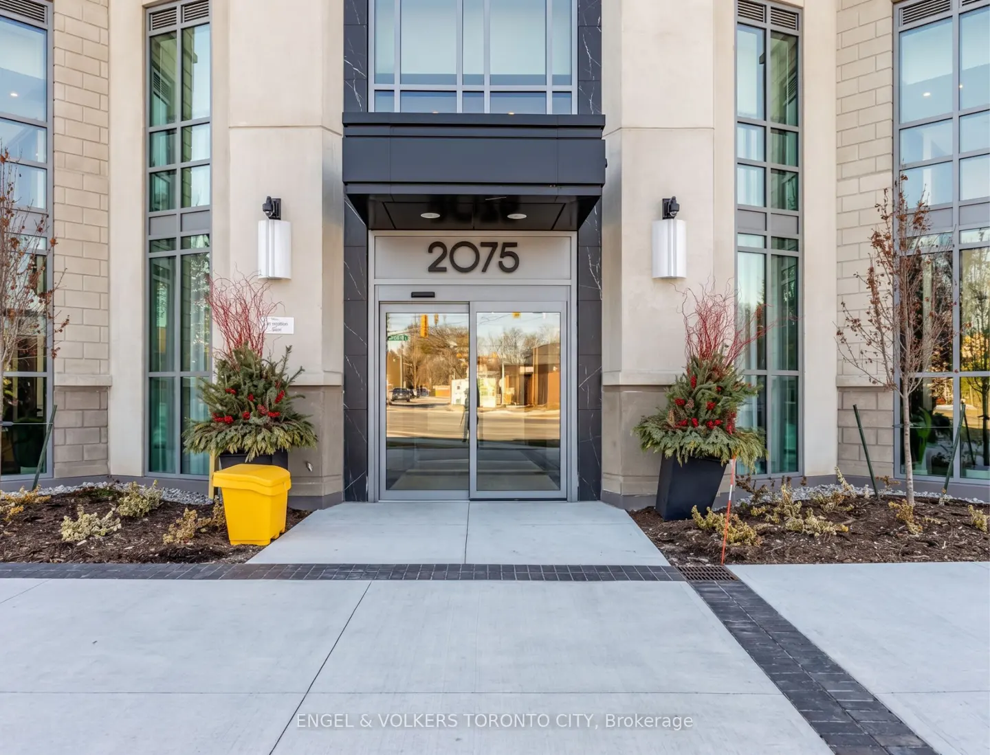 Building entrance with glass doors, number 2075 above. Planters flank the door. Large windows on either side. Concrete walkway.